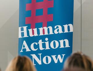 Human Action Now: Engagieren im Humanistischen Verband Berlin-Brandenburg Auf einem Roll-up des Humanistischen Verbandes Berlin-Brandenburg steht auf Blau nach einem roten Hashtag Folgendes in Weiß: „Human Action Now“.