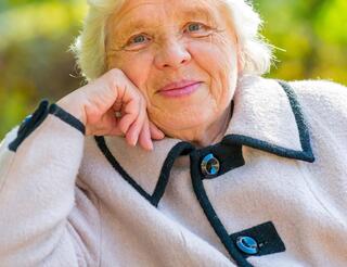 Seniorenberatung Neukölln: Angebot Eine ältere Frau sitzt auf einer Bank und stützt ihren Arme auf der Lehne. Sie lächelt in die Kamera.