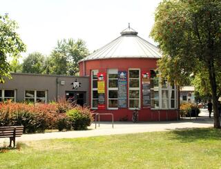 JuKuz Gérard Philipe Gebäude Zu sehen ist das Gebäude des Jugendkulturzentrums Gérard Philipe. Es ist ein flaches Haus mit einer runden Kuppel an der rechten Seite. Davor ist ein grüne Wiese und ein Gehweg.